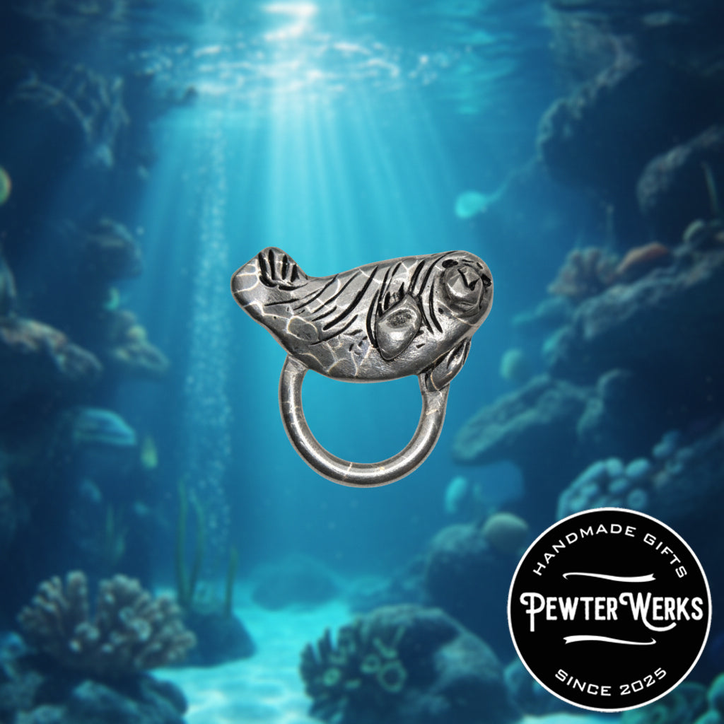 A 'Baby Seal' eyeglass holder swimming amongst the coral in the ocean. PewterWerks logo visible.