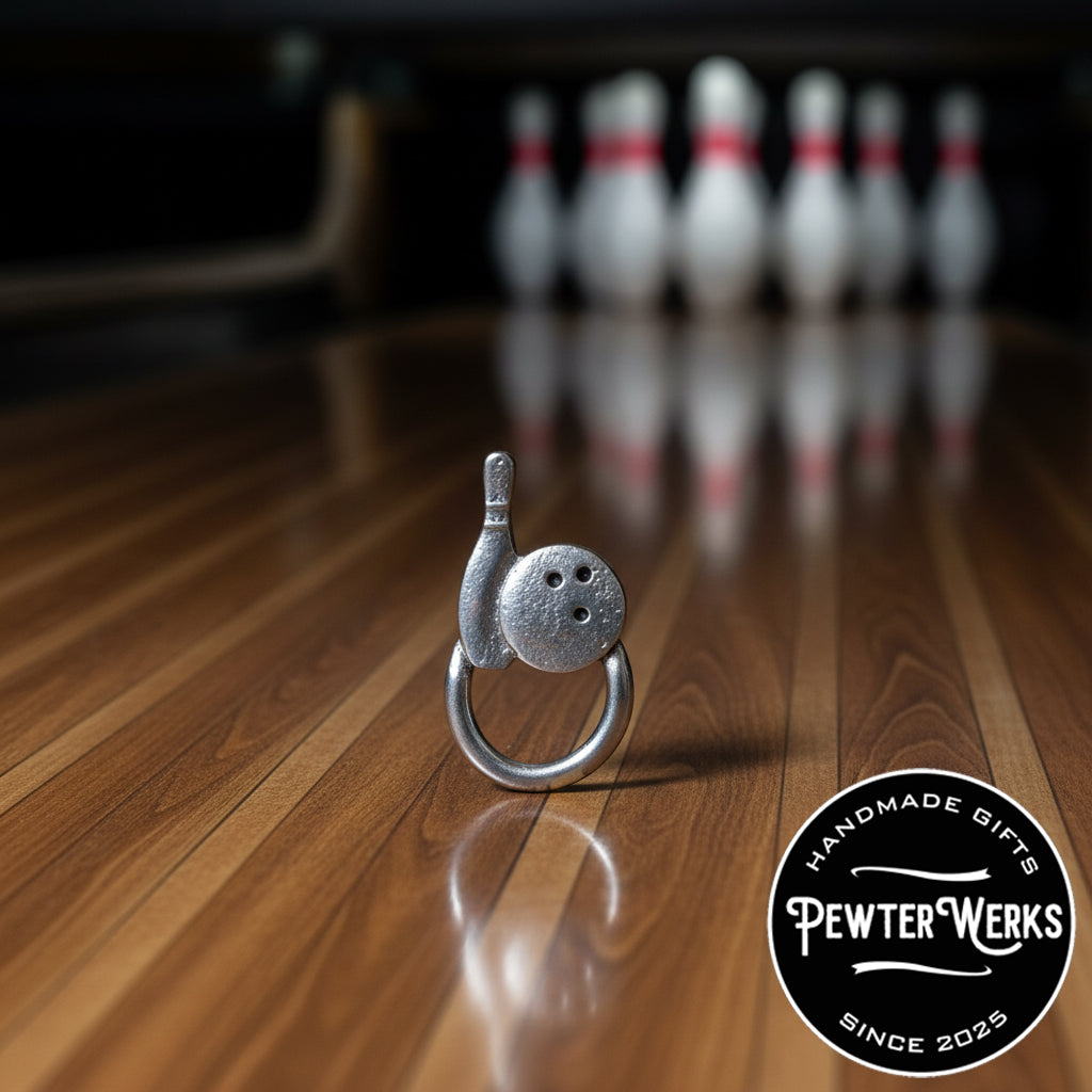 A pewter 'Bowling' eyeglass holder sitting on the hardwood lane in front of the pins. PewterWerks logo visible.