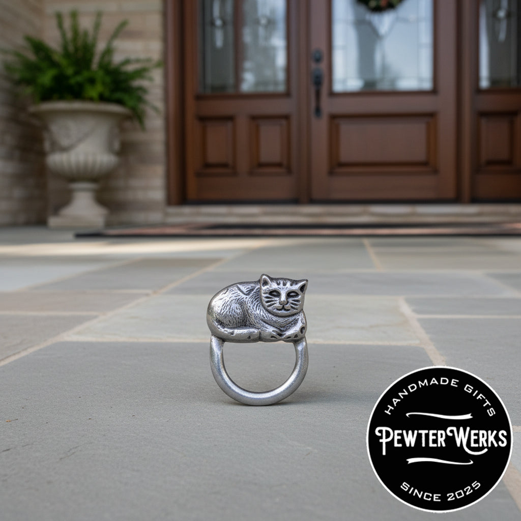 A pewter 'Cat' eyeglass holder sitting outside a house near the front door. PewterWerks logo is visible.