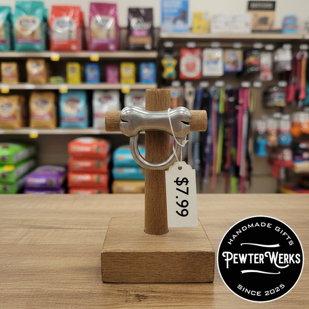 A pewter 'Dog Bone' eyeglass holder on sale in a local dog shop for $7.99. PewterWerks logo visible.