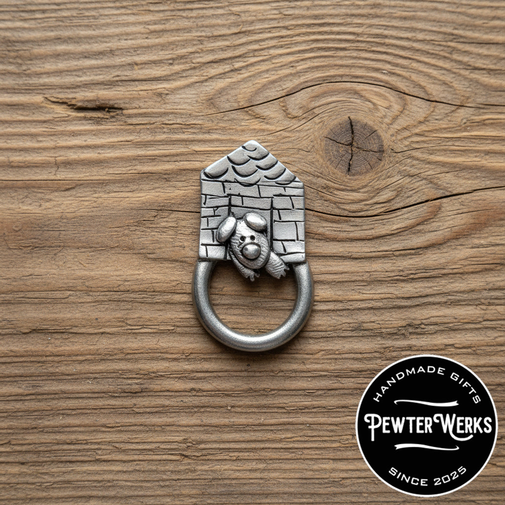 A pewter 'Doghouse' eyeglass holder with dog peeking out laying on an old piece of distressed wood. PewterWerks logo visible.