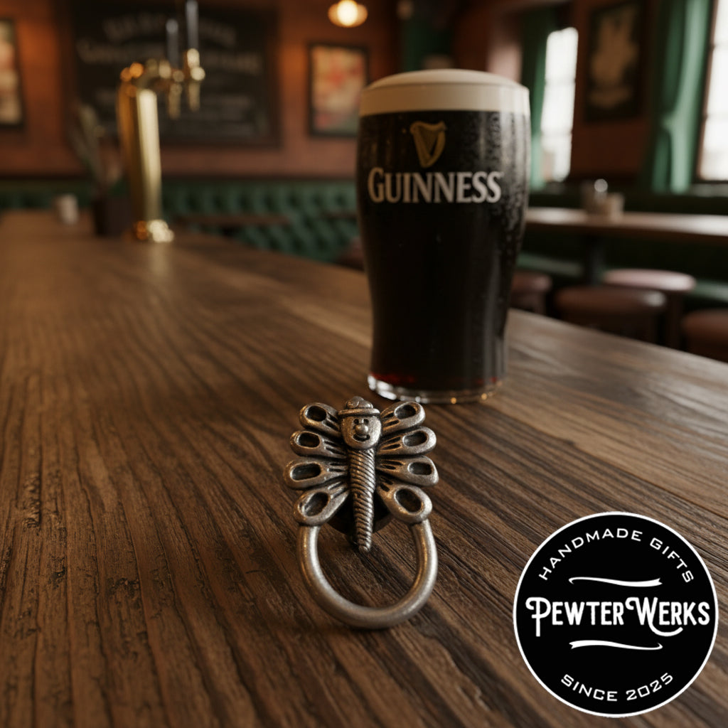 A pewter 'Dragonfly Leprechaun' eyeglass holder sitting on the bar in an Irish pub with a Guinness in the background. PewterWerks logo visible.