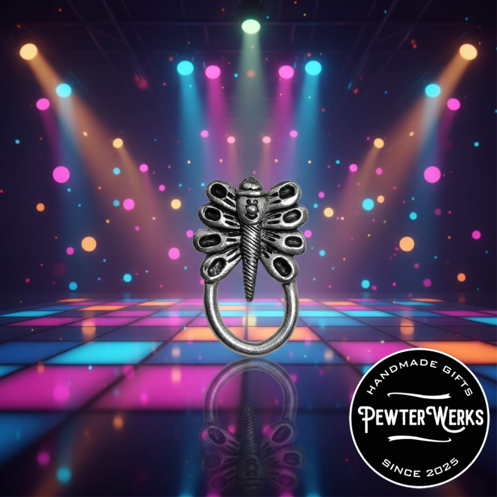 A pewter 'Dragonfly Leprechaun' eyeglass holder out on an exclusive electric dance floor all lit up. PewterWerks logo visible.