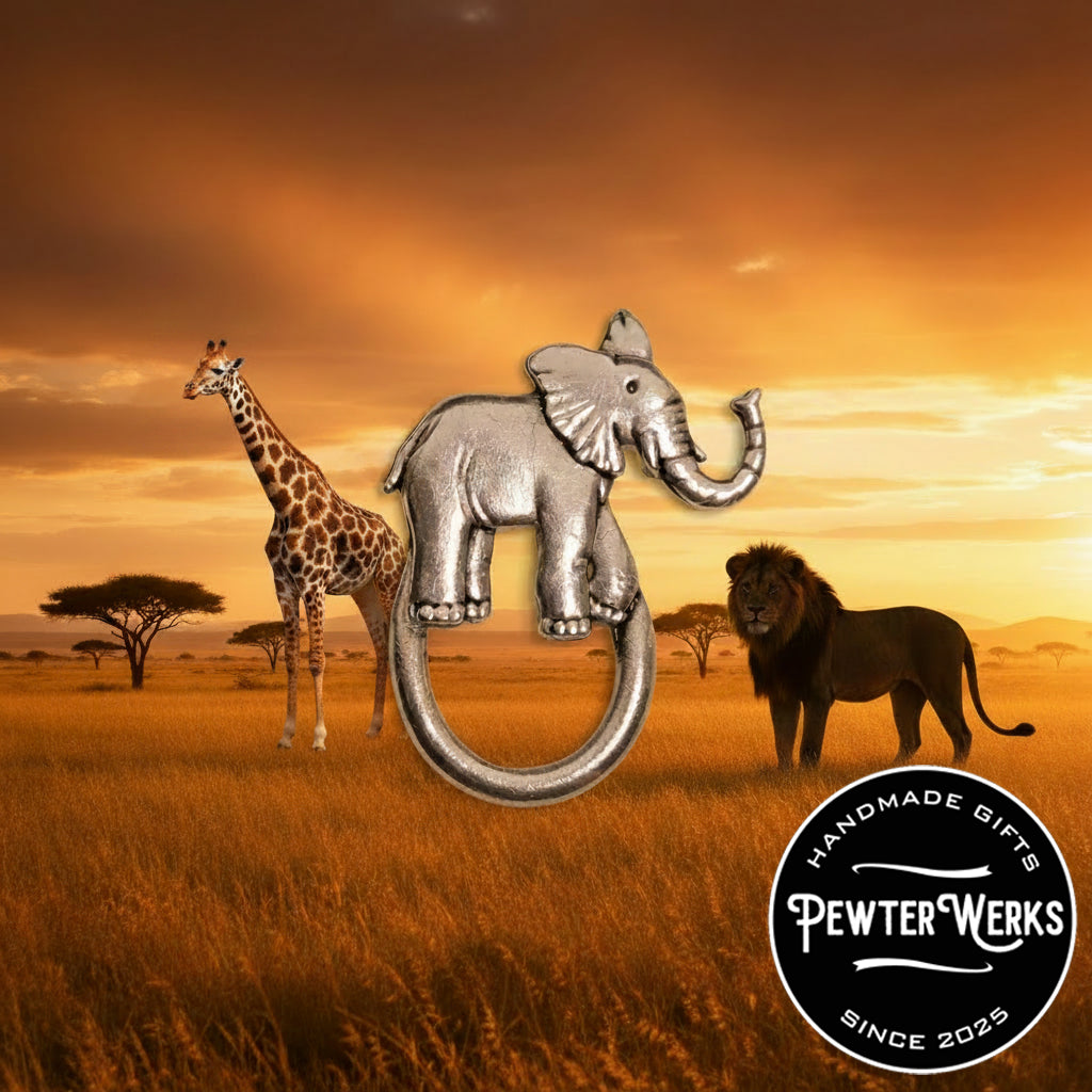 A pewter 'Elephant' eyeglass holder in the Serengeti with a giraffe and a lion in the background. PewterWerks logo visible.