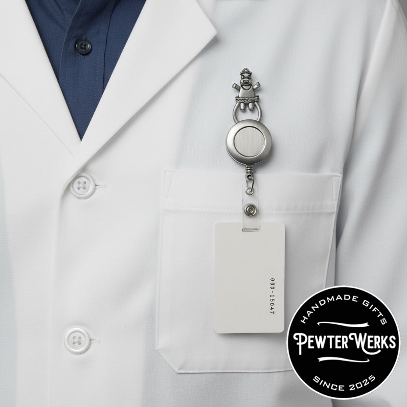 Close-up of a white lab coat with an ID badge holder attached to a 'Dancing Hippo' Eyeglass Holder. PewterWerks logo visible.
