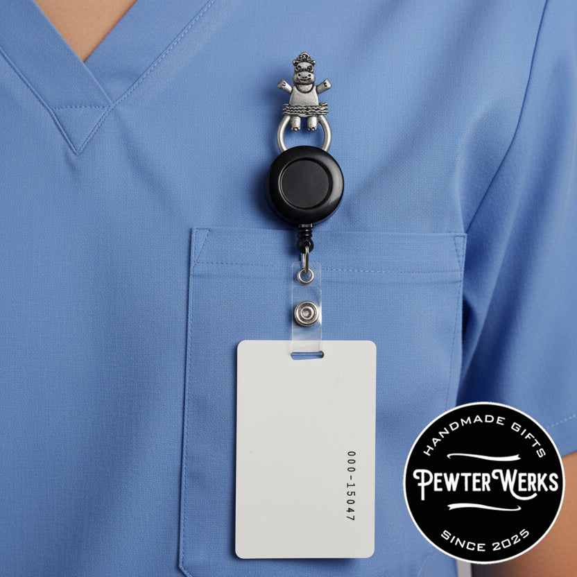 'Dancing Hippo' Badge Holder attached to a badge reel attached to an ID badge attached to blue scrubs. PewterWerks logo visible.